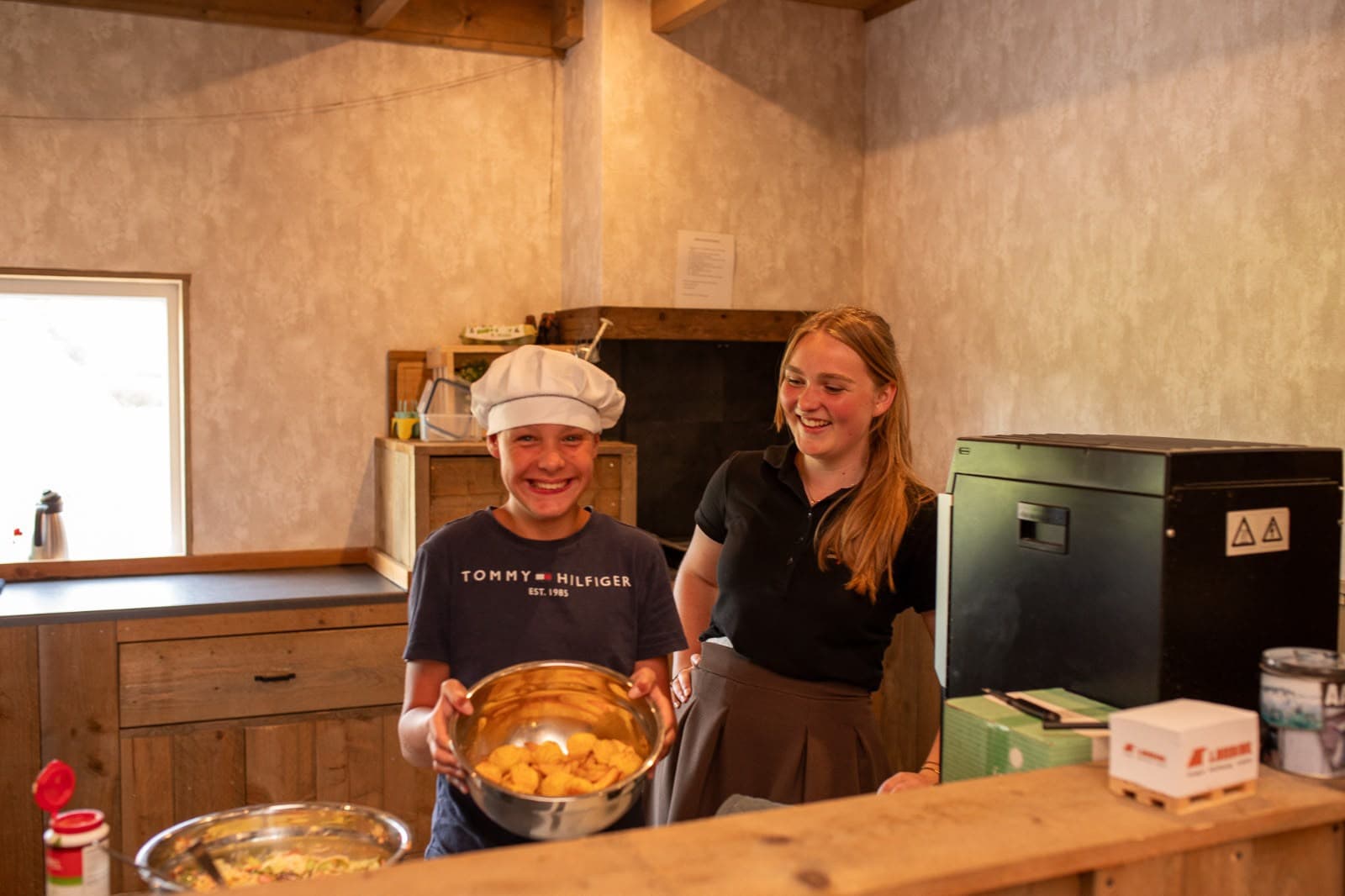 Deelnemer met koksmuts en begeleider lachen samen in de keuken